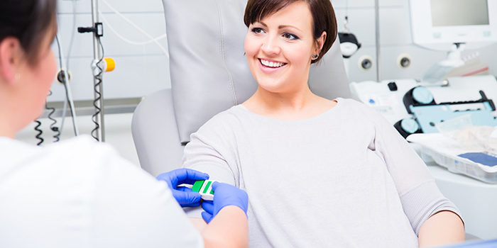 Donatrice sorridente seduta su poltrona mentre un’operatrice applica un laccio emostatico al suo braccio prima della donazione di sangue Donatrice sorridente seduta su poltrona mentre un’operatrice applica un laccio emostatico al suo braccio prima della donazione di sangue