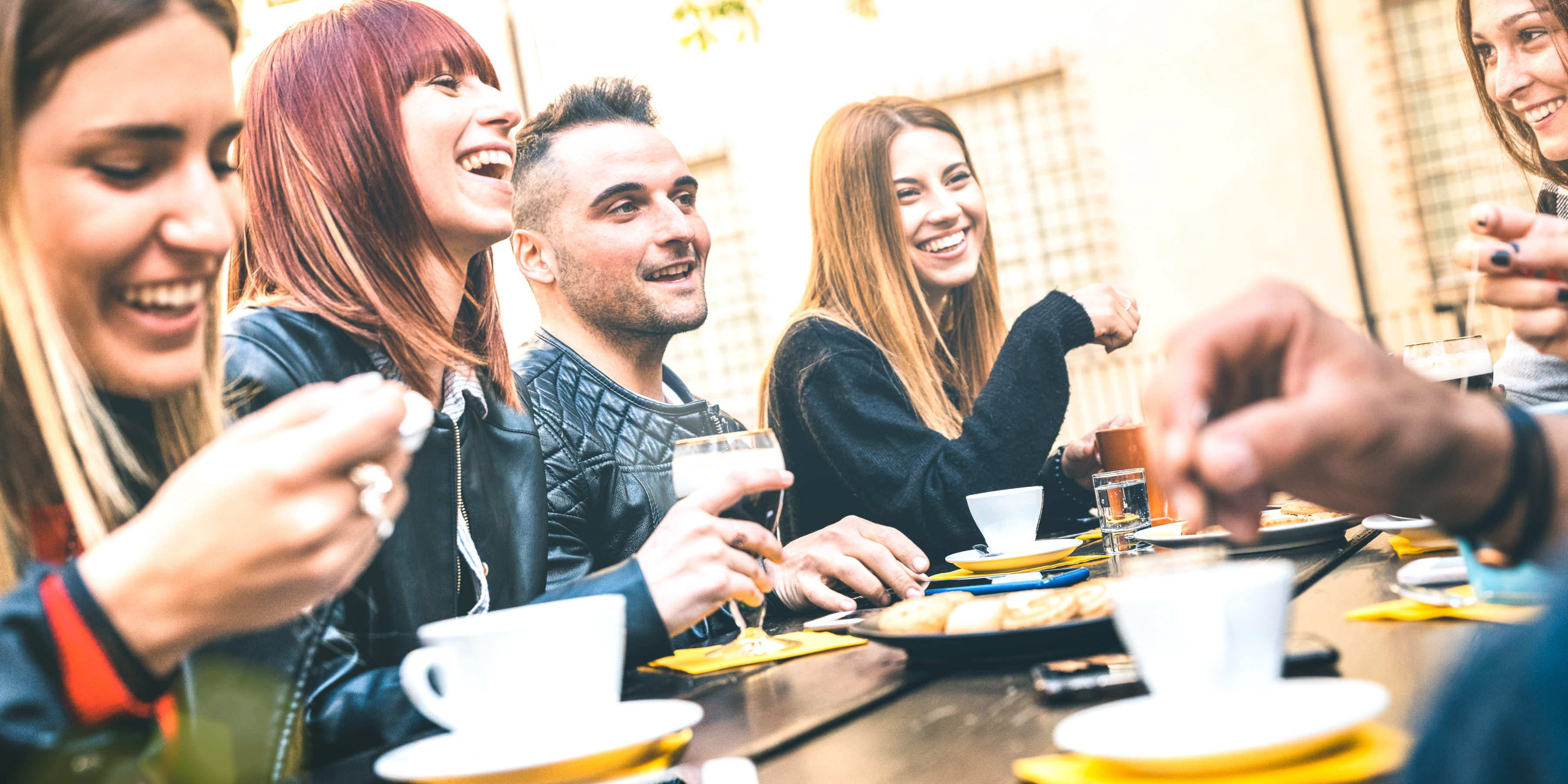 Gruppo di amici seduti a un tavolo all’aperto che ridono e bevono cappuccino Gruppo di amici seduti a un tavolo all’aperto che ridono e bevono cappuccino