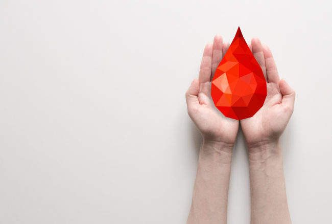 Due mani aperte che sostengono una grande goccia rossa stilizzata a mosaico, simbolo del dono del sangue