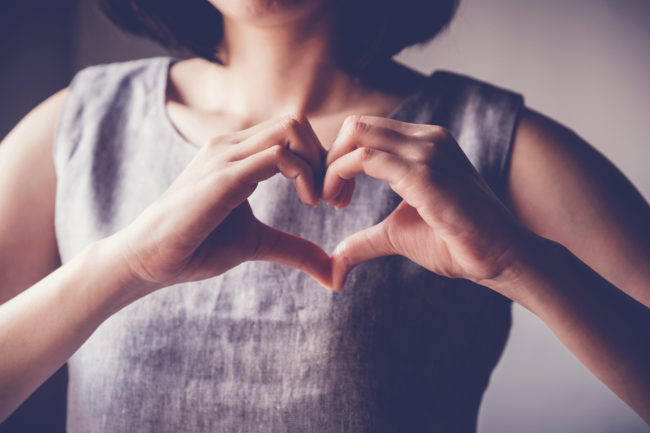Donna che forma un cuore con le mani davanti al petto, simbolo di amore e solidarietà