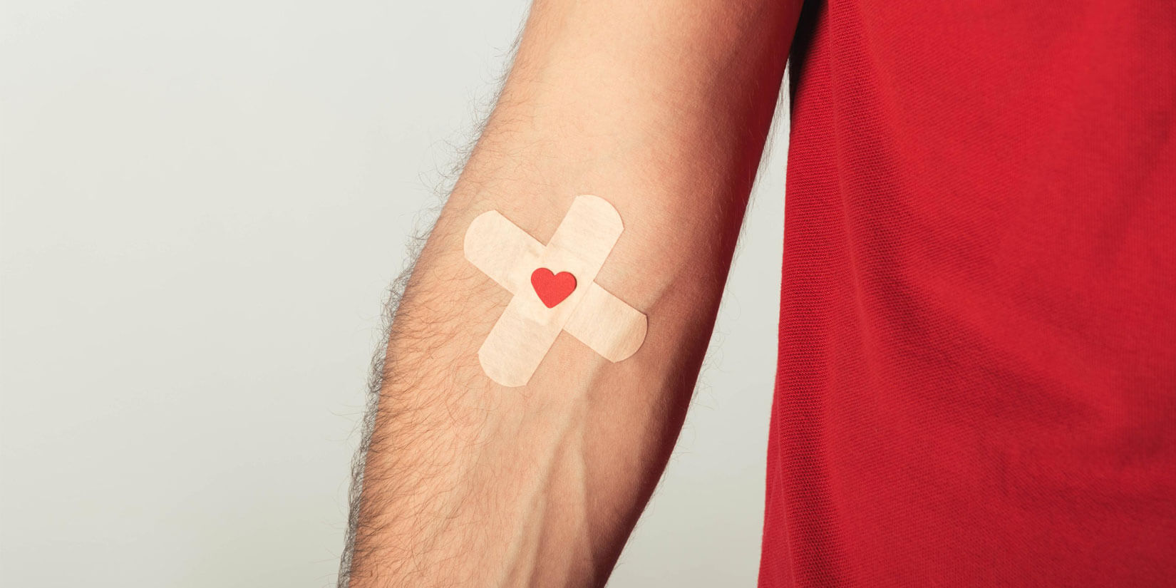 Braccio di un uomo con due cerotti incrociati e un cuoricino rosso sul punto della donazione, simbolo della donazione di sangue